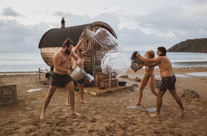 People throwing water over each other after sauna session on beach