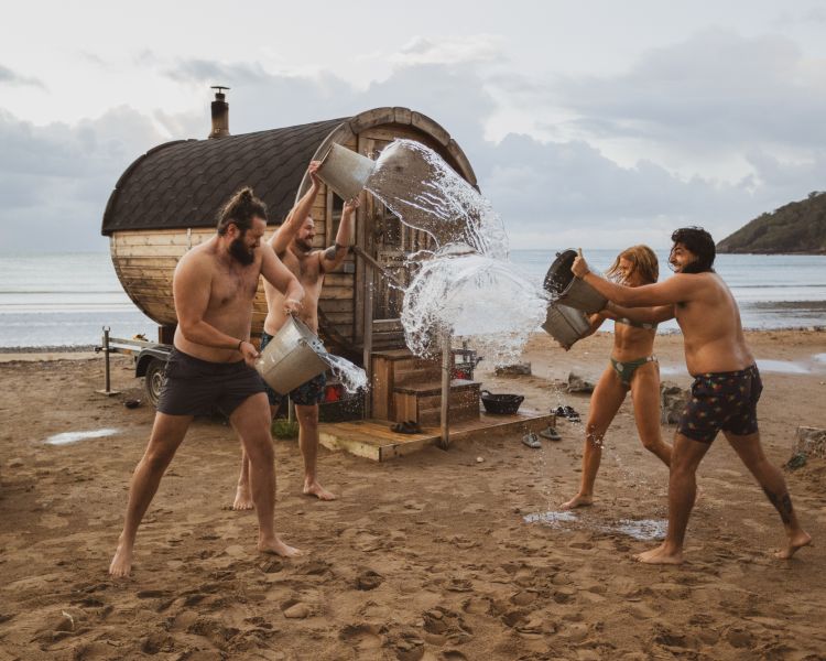 People throwing water over each other after sauna session on beach