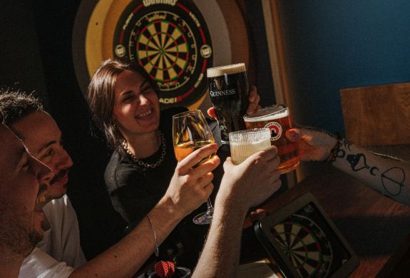 Four people with drinks playing darts at the lucky goat
