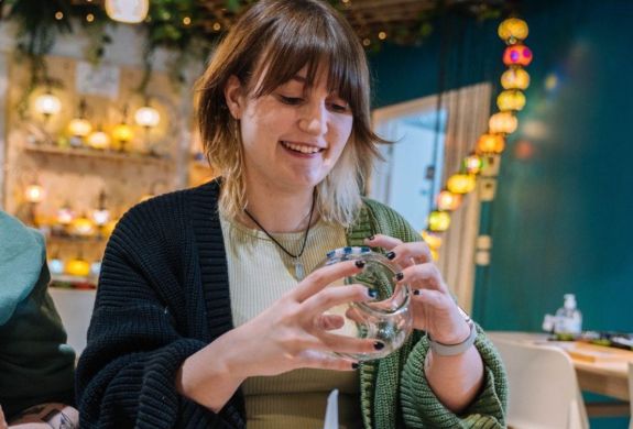 Woman decorating her glass candle holder with coloured mosaic pieces