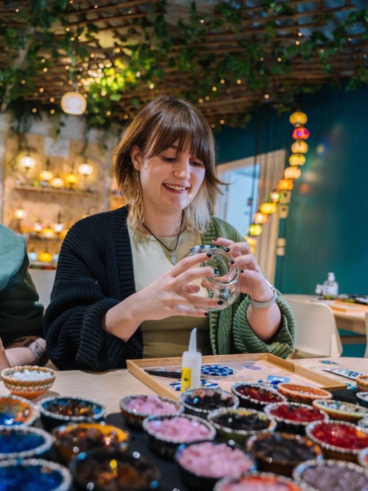 Woman decorating her glass candle holder with coloured mosaic pieces