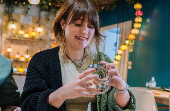Woman decorating her glass candle holder with coloured mosaic pieces