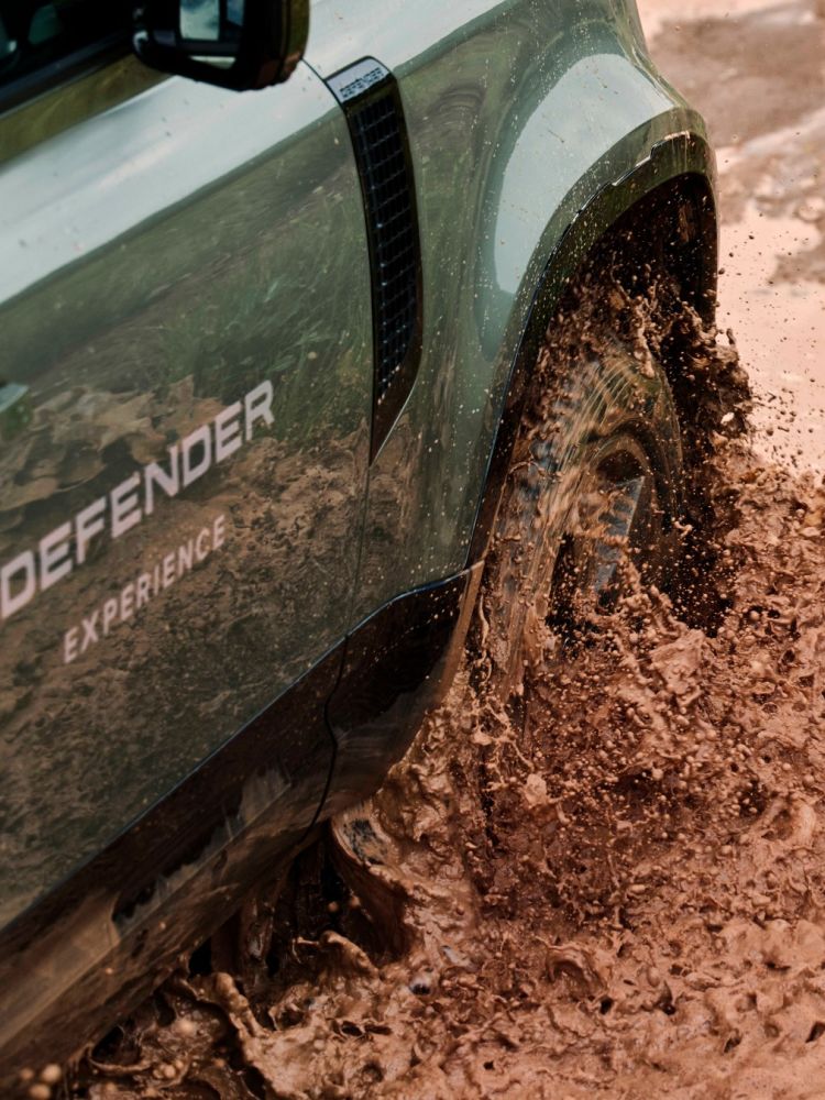 Green land rover defender going through muddy water on driving experience