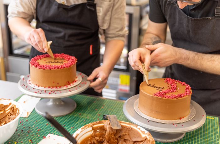 Two people decorating a red velvet cake at cake decorating class