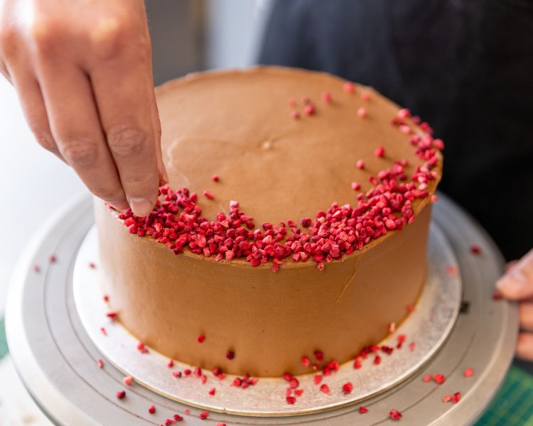 adding dried strawberry pieces to cake at cake decorating class in battersea