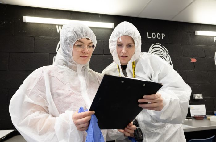 Two people in white hasmat suits reading a clipboard