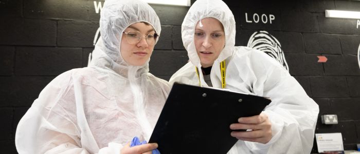 Two people in white hasmat suits reading a clipboard