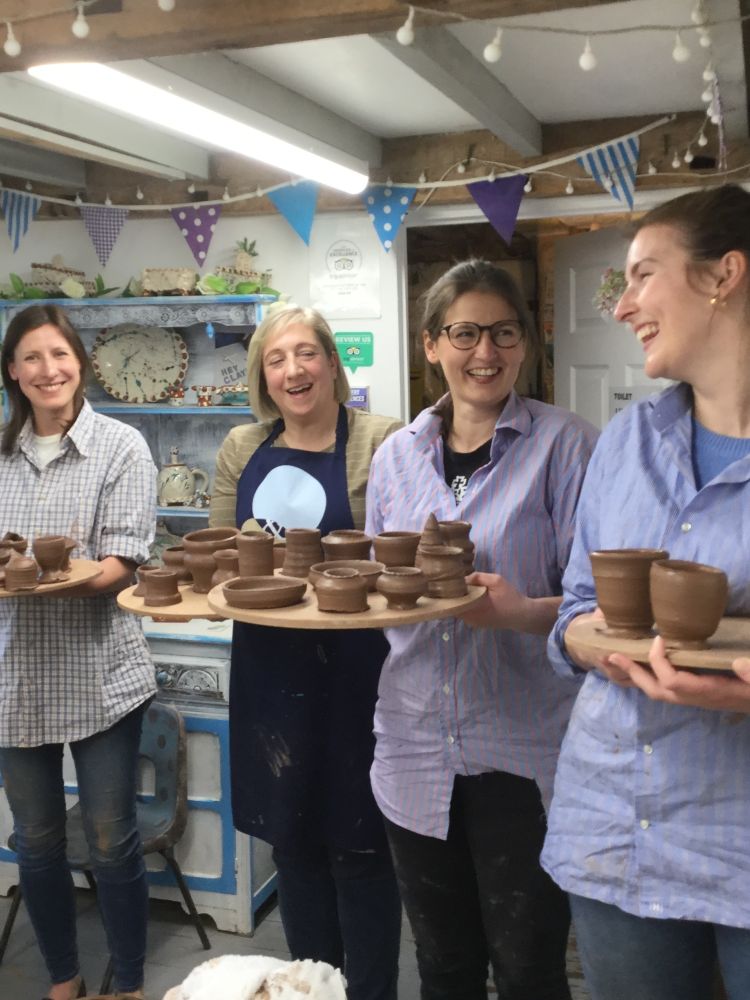 four ladies in a pottery workshop holding boards with their clay creations made during a pottery course experience day.
