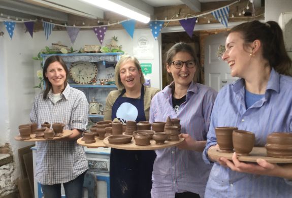 four ladies in a pottery workshop holding boards with their clay creations made during a pottery course experience day.