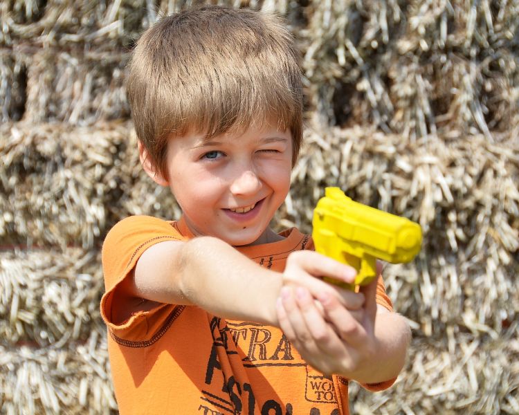 young boy in an orange t-shirt aiming a pretend gun while on a spy camp experience day for kids