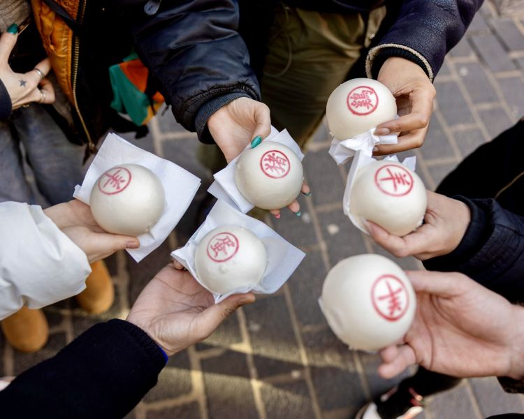 people holding buns with red design on them on food tour through london's chinatown and soho