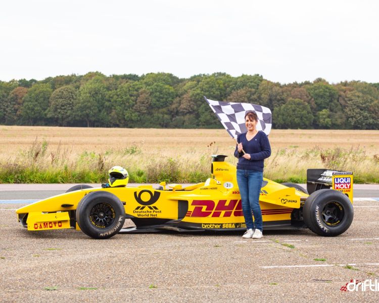 woman holding chequered flag next to f1 jordan car on a f1 car photoshoot and passenger lap experience