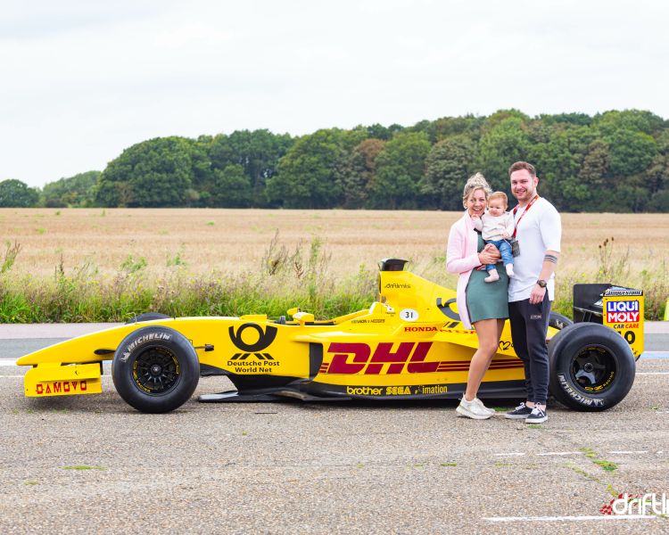 couple holding their baby standing next to f1 jordan car on a f1 car photoshoot and passenger lap experience