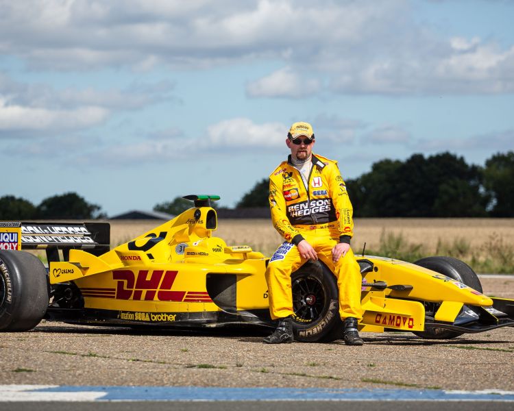 man in yellow driving suit sat on an f1 jordan car on a f1 car photoshoot and passenger lap experience