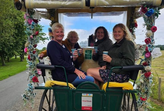 four ladies with takeaway drinks sitting in a carriage decorated with flowers on a horse carriage ride experience