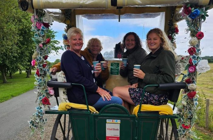 four ladies with takeaway drinks sitting in a carriage decorated with flowers on a horse carriage ride experience