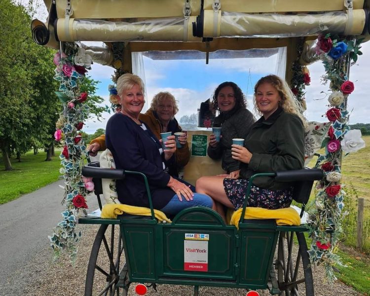 four ladies with takeaway drinks sitting in a carriage decorated with flowers on a horse carriage ride experience