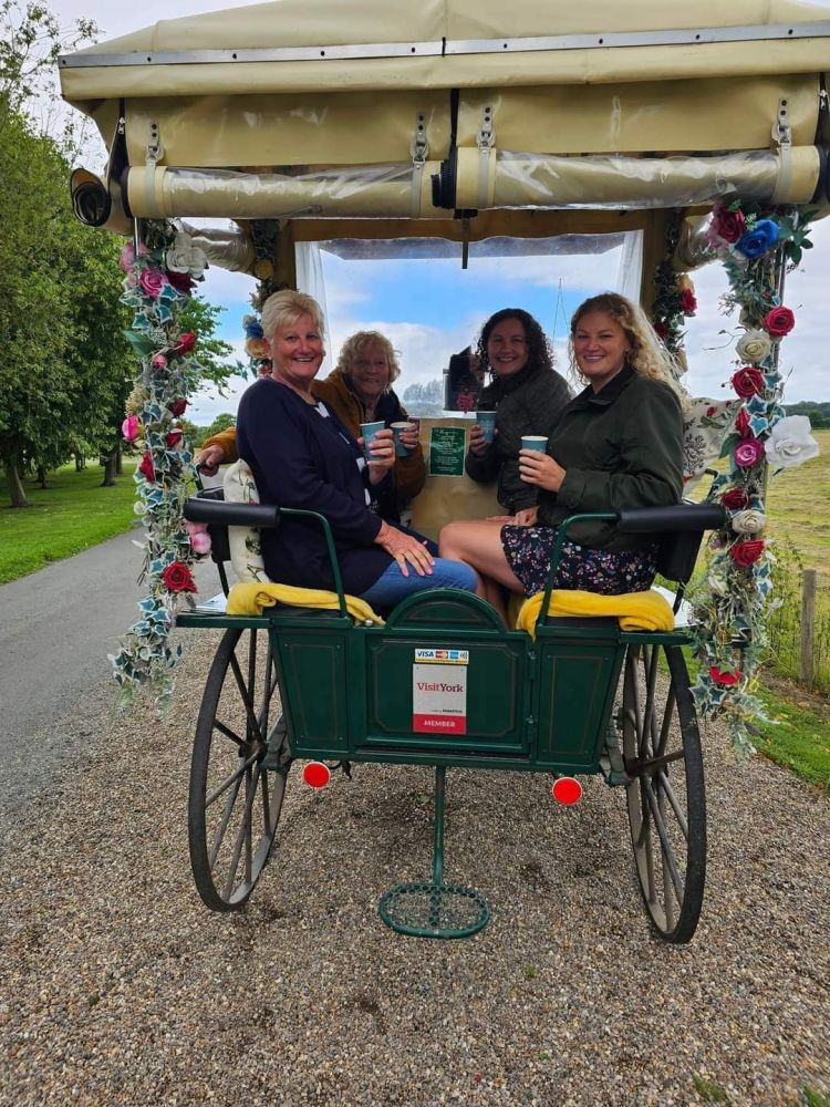 four ladies with takeaway drinks sitting in a carriage decorated with flowers on a horse carriage ride experience