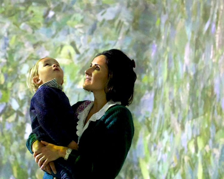 woman holding a child while looking at the paintings at the frameless immersive art exhibition in london