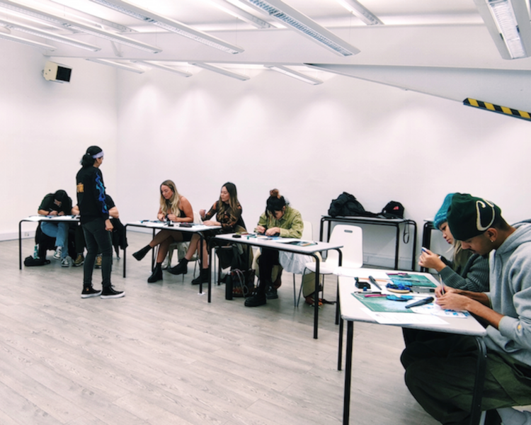 a row of desks with people working at a gemstone jewellery making workshop with stööki