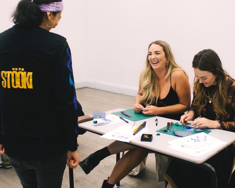 people at a workbench receiving guidance during a gemstone jewellery making workshop with stööki