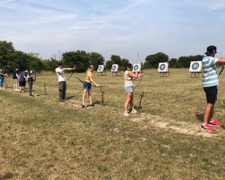 Row of people aiming at targets on archery experience