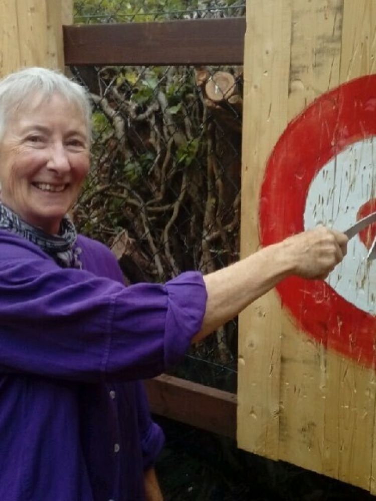 woman posing for photo with an axe thrown at a target on an axe throwing experience day