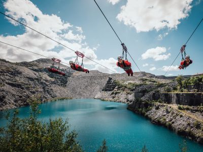 people on the zip lines at zip world velocity in wales going over the quarry lake