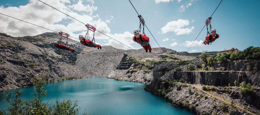 people on the zip lines at zip world velocity in wales going over the quarry lake