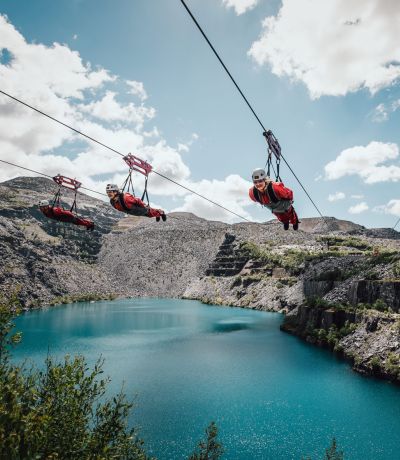 people on the zip lines at zip world velocity in wales going over the quarry lake