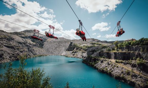 people on the zip lines at zip world velocity in wales going over the quarry lake