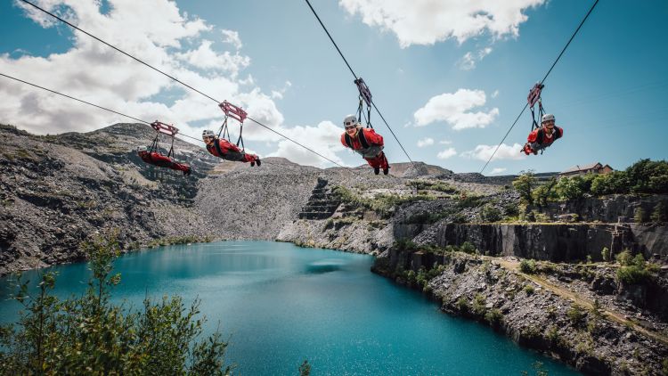 people on the zip lines at zip world velocity in wales going over the quarry lake