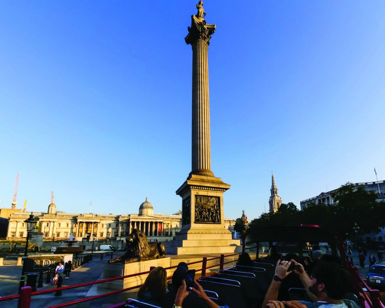 a sightseeing tour bus going past trafalgar square in london