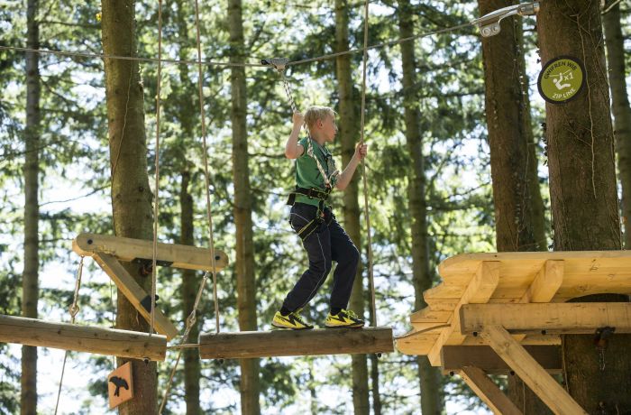 a child making their way across an obstacle course high in the trees on a tree hoppers experience at zip world
