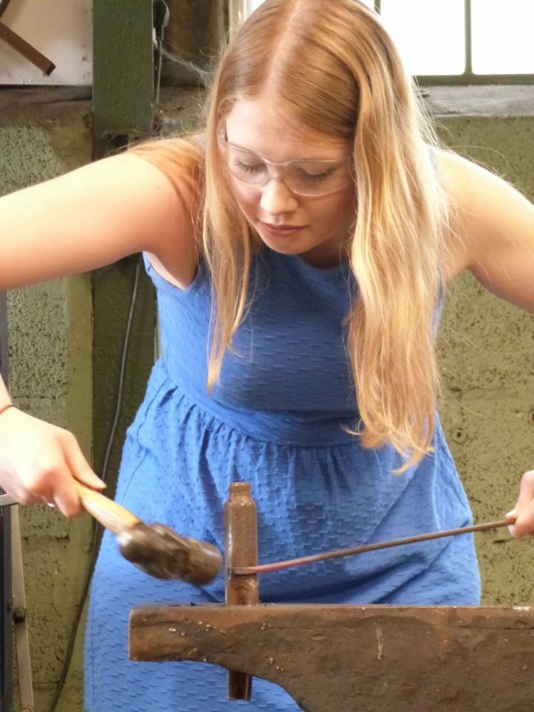 woman in a forge shaping metal on a just for fun blacksmith experience