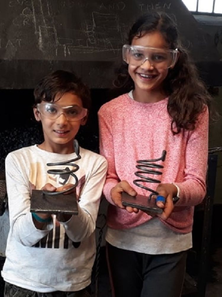 two young children holding metal candle holders made on a just for fun blacksmith experience