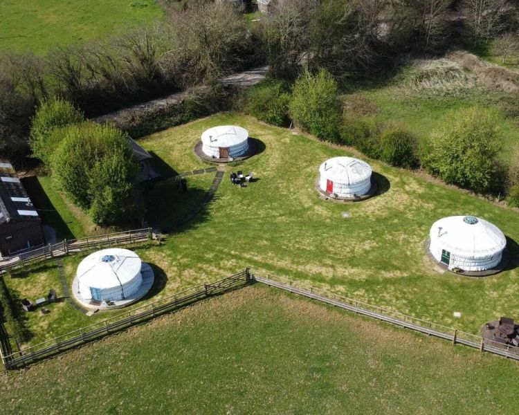 an aerial view of the devon yurts complex with shepherds hut and four white round yurts