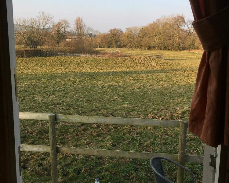 the view of fields outside the door of a shepherds hut set in the grounds of devon yurts