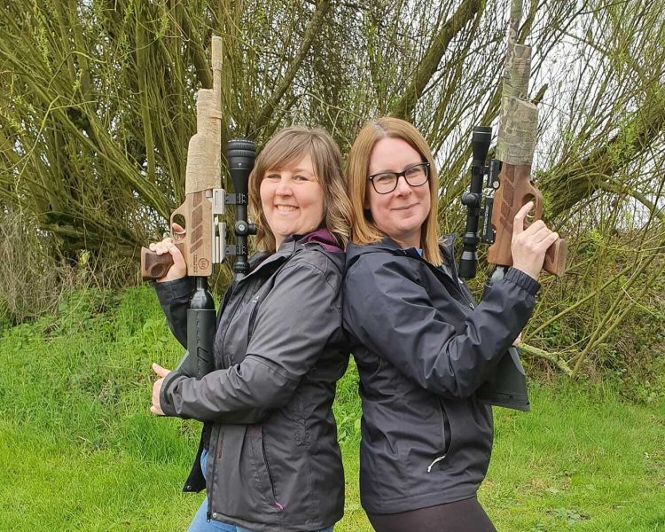 two women standing back to back holding air rifles on an air rifle shooting experience day