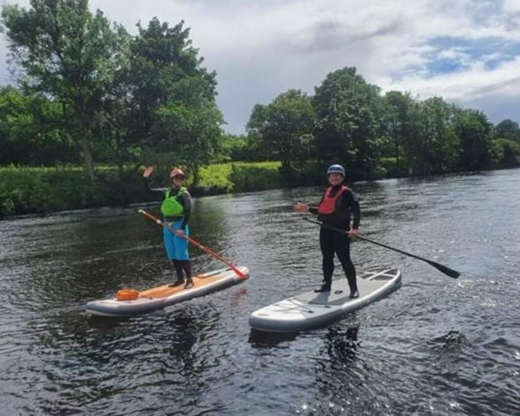 2 people paddle boarding on a river on an all day stand up paddle boarding experience day