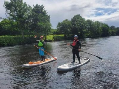 2 people paddle boarding on a river on an all day stand up paddle boarding experience day