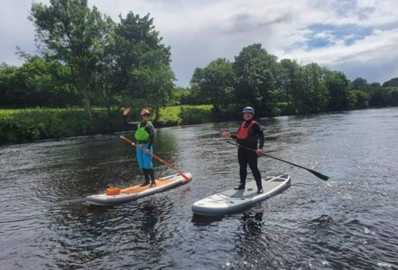 2 people paddle boarding on a river on an all day stand up paddle boarding experience day