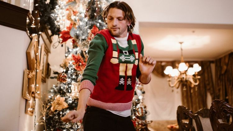 Man dancing wearing a christmas jumper infront of a christmas tree