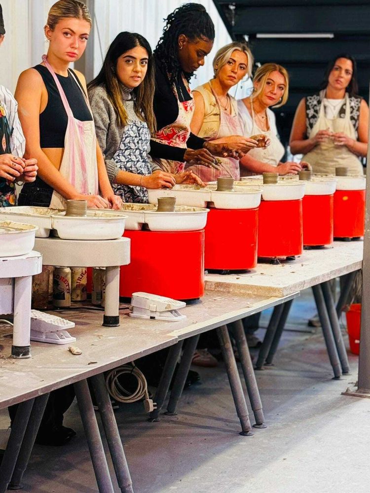 a line of people standing in front of potter's wheels ready to start a pottery experience in london