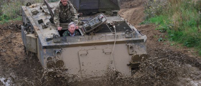 a military tank being driven through a muddy puddle on a tank driving experience day
