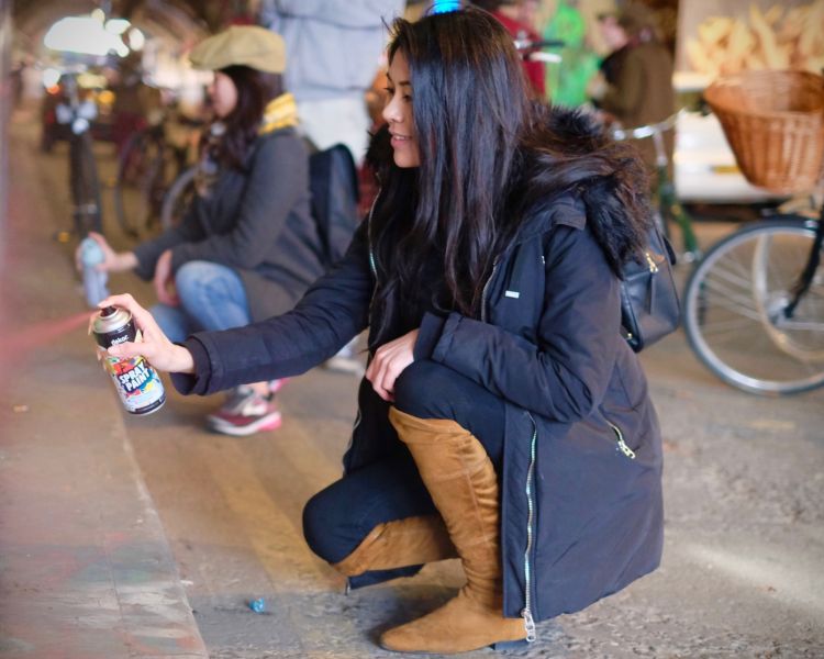 woman holding a spray paint can doing graffiti in the banksy tunnel in london