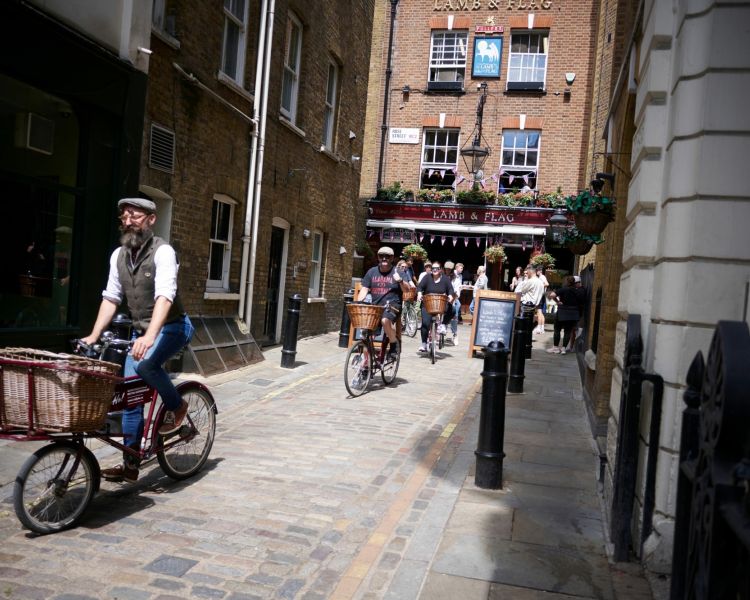 group of people riding vintage bicycles past the lamb and flag pub on a bike sightseeing tour