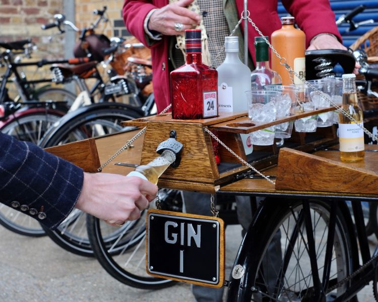 person opening a bottle on the back of a bicycle loaded with bottles of gin on a gin bike tour