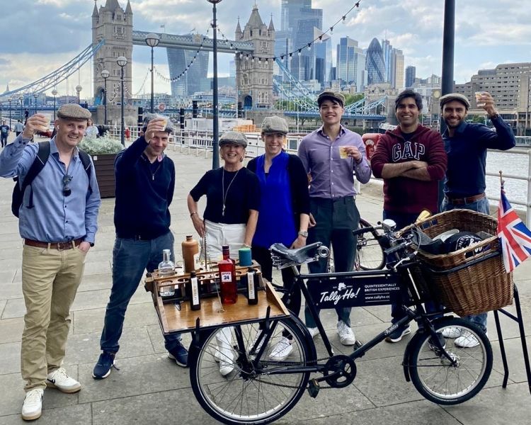 group of people standing next to vintage bicycles in front of tower bridge on a gin bike tour