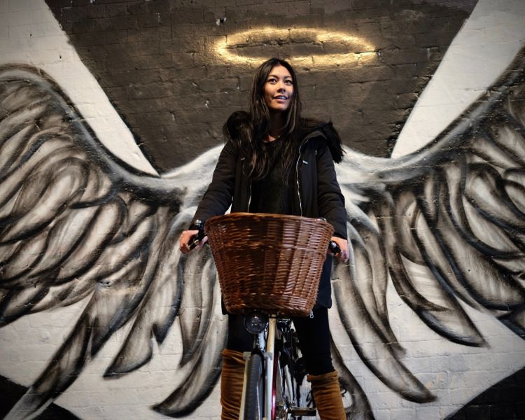 a woman on a vintage bicycle photographed in front of a pair of angle wings on a visit to the banksy tunnel in london as part of a bike tour